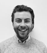 Lloyd Damron Associate Director smiling in grey jumper with black and white filter over image